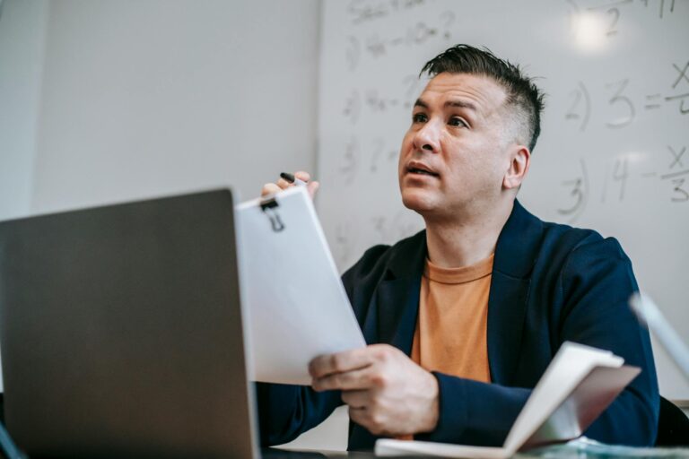Educator discussing concepts during an online session, sitting at a desk with a laptop.